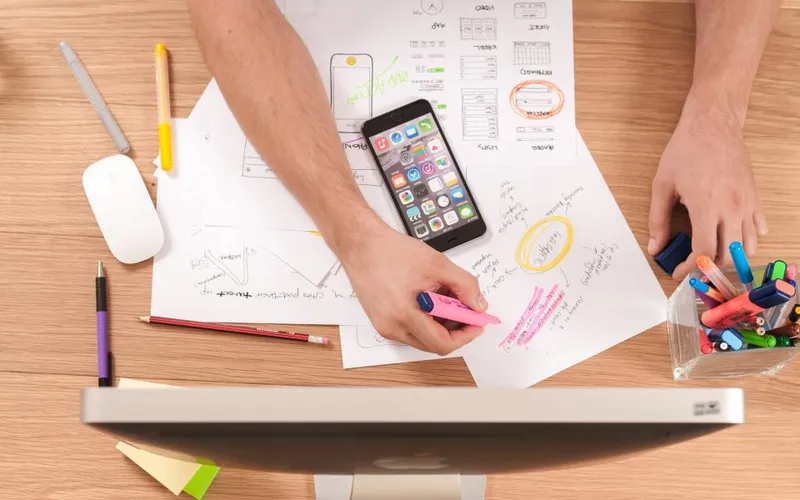 Designer sketching mobile app interface layouts next to an iPhone